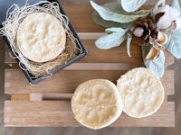 two soaps on a wooden tray with sprigs of sage and eucalyptus