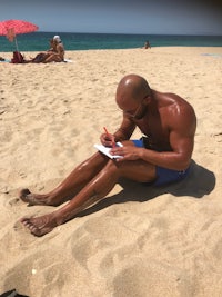 a man sitting on the sand writing a note