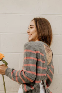 a woman holding a flower while wearing a grey striped sweater