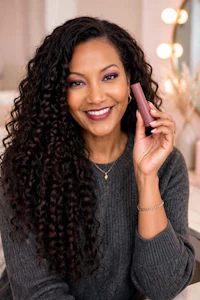 a woman with curly hair holding a lipstick in front of a mirror