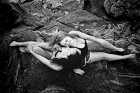 a black and white photo of two women laying on rocks