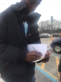 a young man signing a piece of paper in a parking lot