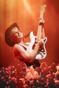 a man in a cowboy hat plays an electric guitar in front of a crowd