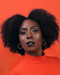 a black woman with afro hair is posing in front of an orange background