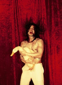 a man holding a duck in front of a red curtain