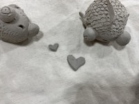 two clay pigs with hearts in their mouths