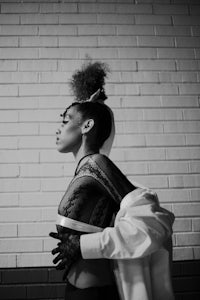 a black and white photo of a woman leaning against a brick wall