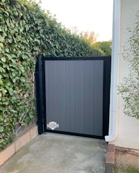 a driveway gate with a black gate and bushes
