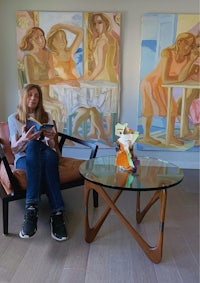 a woman sitting in a chair in front of paintings