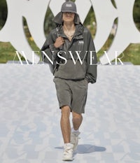 a man walking down the runway with a hat and shorts