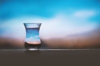 a glass of water sitting on a table with a blue sky behind it