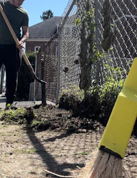 a man with a yellow broom and a shovel in front of a fence