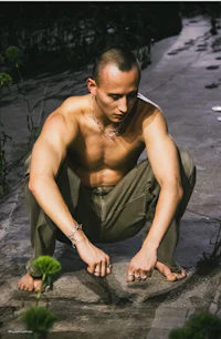 a shirtless man crouching down in front of some plants