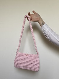 a person holding up a pink crocheted bag