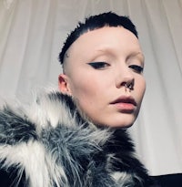 a woman with a shaved head wearing a fur coat