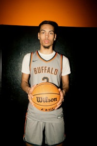 a young man holding a basketball in front of an orange wall