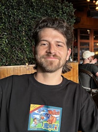 A handsome man with a modern mullet wearing a black shirt with a stunning smile