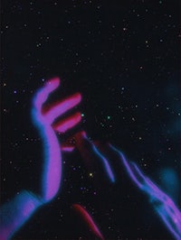 a person's hand reaching out to a starry sky