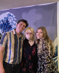 three people posing for a photo in front of a mural