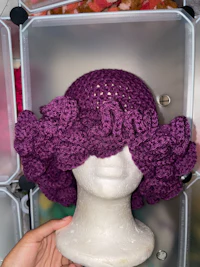 a person holding a purple crocheted hat in a box
