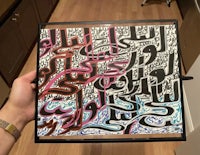 a person holding a piece of art with arabic calligraphy on it