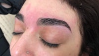 a woman's eyebrows are being tattooed by a tattoo artist