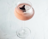 a glass of pink gin with ice and a flower