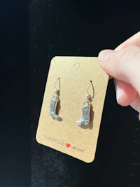 a hand holding a pair of silver cowboy boots earrings