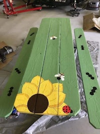 a wooden picnic table with ladybugs and sunflowers painted on it