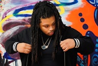 a man with dreadlocks standing in front of a colorful wall