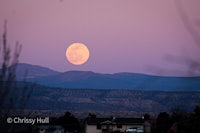 a full moon rising over a mountain
