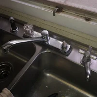 a kitchen sink with two faucets and a window