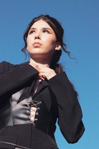 a woman in a black dress posing in front of a blue sky
