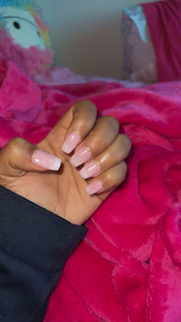 a woman's hand holding a pink teddy bear on a bed