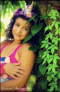 a girl in a pink dress leaning against a tree