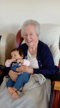 an elderly woman sitting in a chair holding a baby