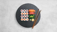 japanese sushi on a black plate with chopsticks