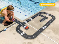 a boy is playing with a toy car track near a pool