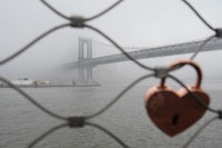 a heart shaped lock on a fence in front of the manhattan bridge