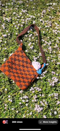 an orange and brown crocheted bag laying in the grass