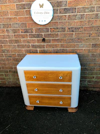 a white and wooden chest of drawers in front of a brick wall