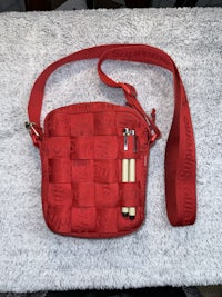 a red cross body bag with a pen on it