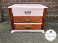 a pink nightstand with two drawers and brass handles