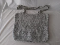 a grey crocheted bag sitting on a bed
