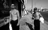 two shirtless men standing on a sidewalk