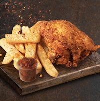 a chicken with fries and sauce on a wooden board
