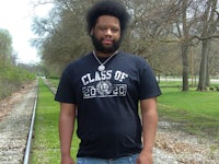 a man wearing a black t - shirt standing next to a train track