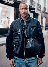 a man in a black jacket and jeans standing on a street