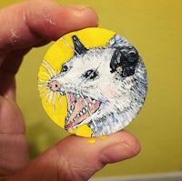 a person is holding a small opossum on a yellow background