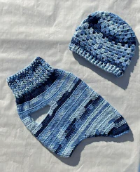 a blue crocheted sweater and hat on a white surface